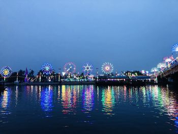 Illuminated city by river against clear sky at night