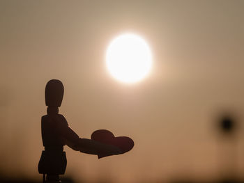 Silhouette wooden figurine with heart shape against bright sun in orange sky