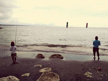 Rear view of men on beach against sky