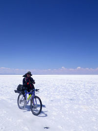 Mid adult man with bicycle standing at salar de uyuni against blue sky