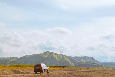 Car on road by field against sky