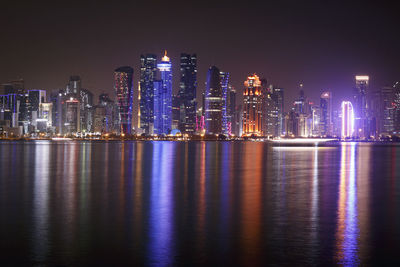 Illuminated buildings by river against sky at night