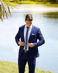 Young man standing by lake against trees