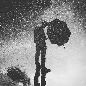 Upside down image of man standing with reflection in puddle on street
