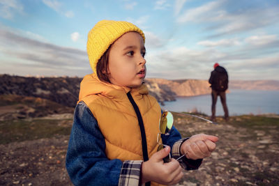 Boy child walks on a mountain in autumn in a yellow vest and a hat