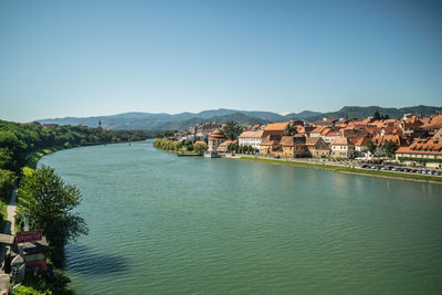 Scenic view of river by buildings against clear blue sky