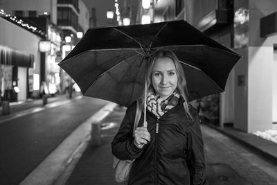 Portrait of smiling woman holding umbrella at night during rainy season