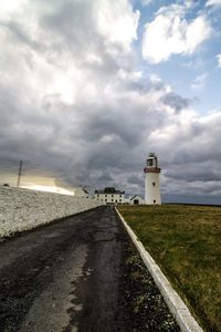 Road leading towards lighthouse amidst buildings against sky