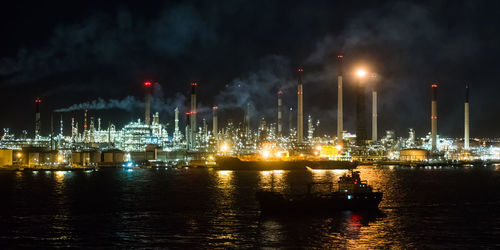 Illuminated factory by lake against sky at night