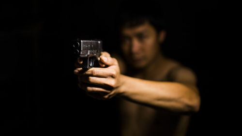 Young man holding gun against black background
