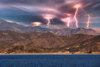 Firework display over sea by mountains against sky