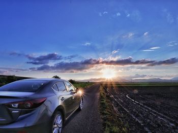 Cars on road amidst field against sky during sunset