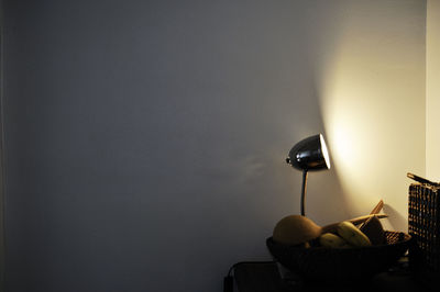 Illuminated lamp on table against wall at home