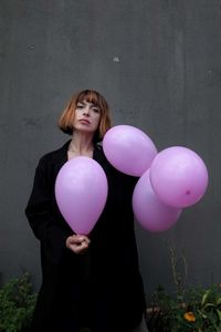 Woman with pink balloons standing against wall
