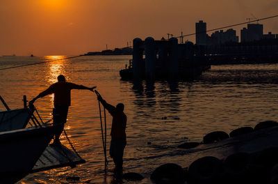 Silhouette fishermen at beach against sky during sunset