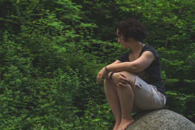 Side view of young woman sitting in forest