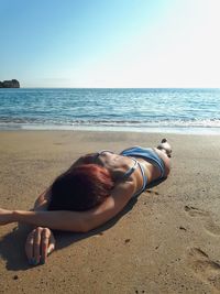 Woman lying on sand at beach against clear sky