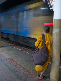 Rear view of monk standing by column against moving train at station