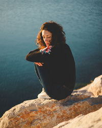 Young woman sitting on rock by sea