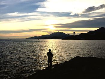 Silhouette man standing by sea against sky during sunset