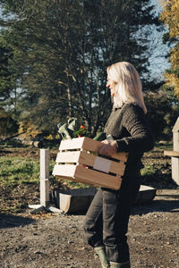 Side view of mature woman carrying crate full of vegetables at farmer's market