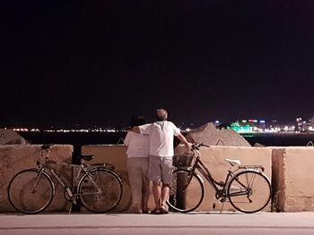 Rear view of man with bicycle standing at night