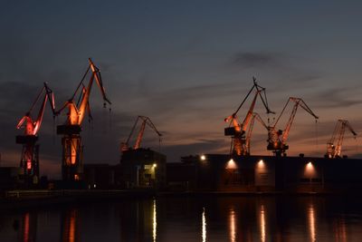 Cranes at commercial dock against sky at night