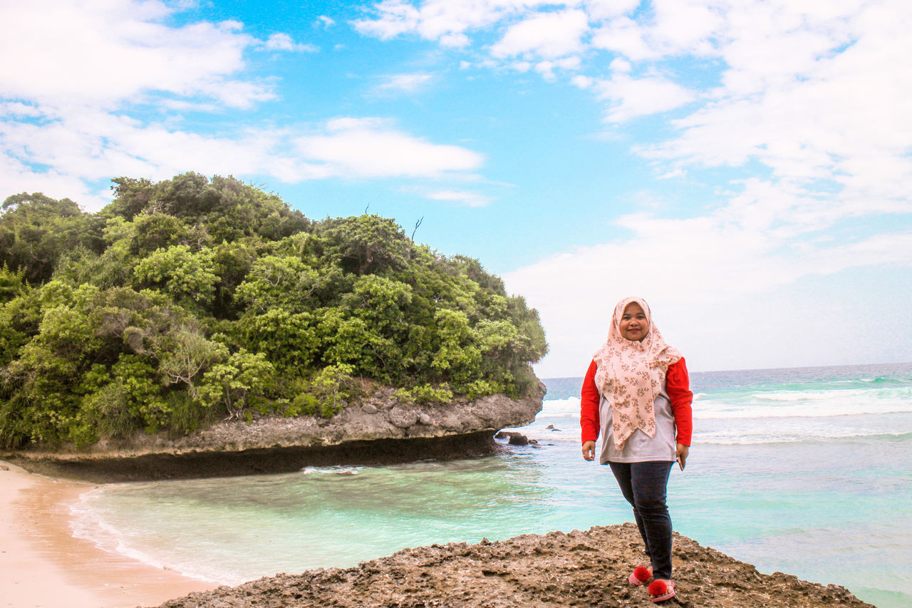 water, real people, sky, full length, one person, beauty in nature, lifestyles, leisure activity, land, beach, standing, sea, scenics - nature, tree, young adult, cloud - sky, plant, day, casual clothing, outdoors