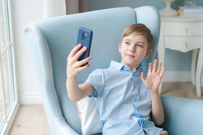 Boy blogger talking to followers looking at smartphone screen and showing hand