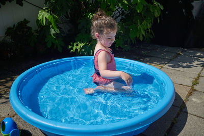 Cute toddler playing in the water basin in the backyard