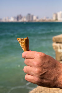 Close-up of hand holding ice cream cone against sea