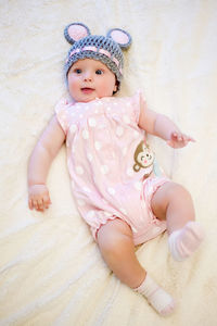 Baby girl lying on her back and smiling on the bed in pink clothes and hat with ears