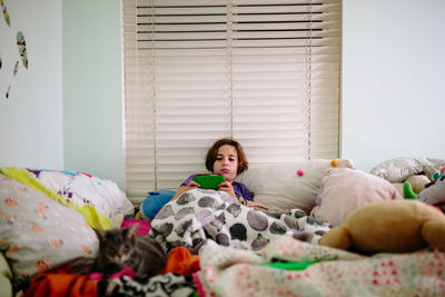 Teen girl laying in bed with her cat and her handheld video game