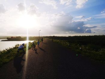 People on road amidst field against sky