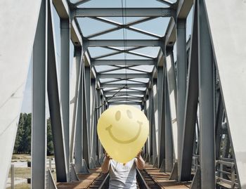 Man holding smiley face balloon on railway bridge