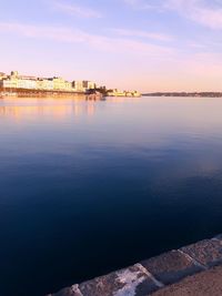 Scenic view of lake by buildings against sky during sunset