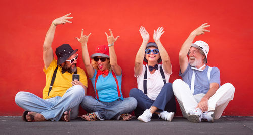 Cheerful friends with arms raised sitting against red wall