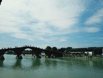 Bridge over river in city against cloudy sky