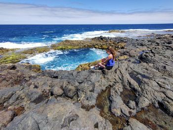 High angle view of woman sitting on rock at sea