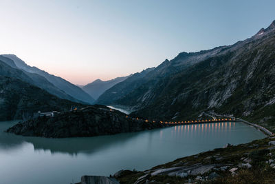 Scenic view of dam by mountains during sunset