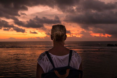Rear view of woman standing by sea against dramatic sky