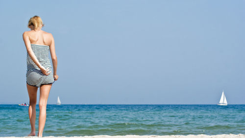 Full length of woman standing in water at beach against clear sky