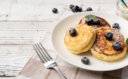 Cottage cheese pancakes served with curd and blueberries, high angle view on wooden background