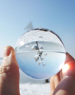 Close-up of hand holding crystal ball against clear sky