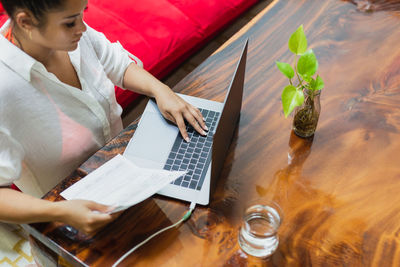 Rear view of woman using digital tablet while sitting on table