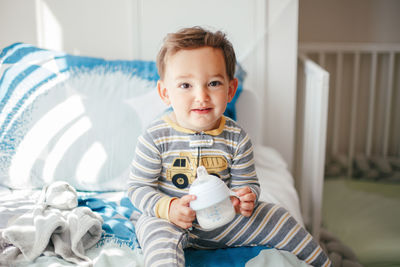 Cute adorable caucasian kid boy sitting on bed drinking milk from kids bottle. healthy eating 