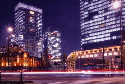 Illuminated light trails on city street by buildings at night