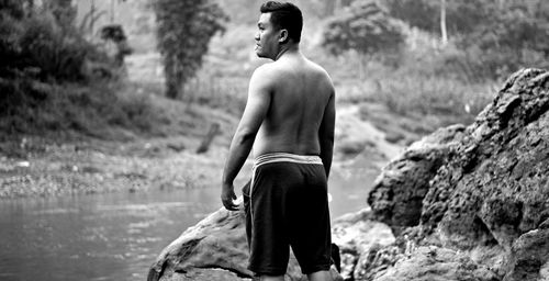 Rear view of shirtless man standing by river