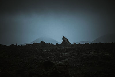 Silhouette rocks on land against sky at dusk