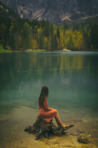 Woman in orange dress sitting on a log on the shore of a lake, italy iii